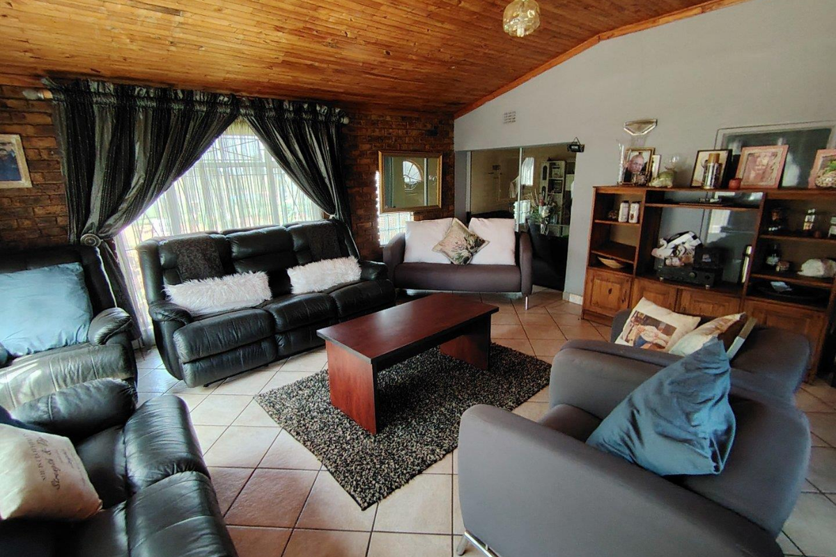 Spacious living room featuring a warm timber tongue and groove ceiling, exposed brick accent wall, and neutral tiled flooring with access to the outdoors.