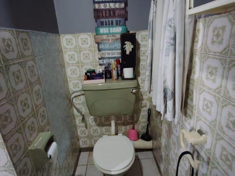 A compact bathroom featuring dated ceramic wall tiles, a standard toilet with a cistern, and a bidet spray fixture.