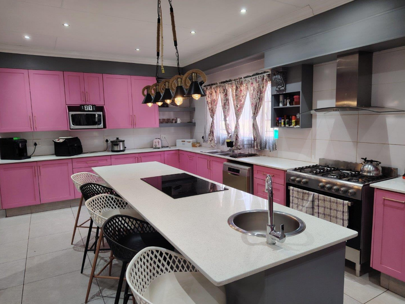 Spacious kitchen featuring pink cabinetry, a large central island with a gas hob and prep sink, quartz countertops, and modern stainless steel appliances.