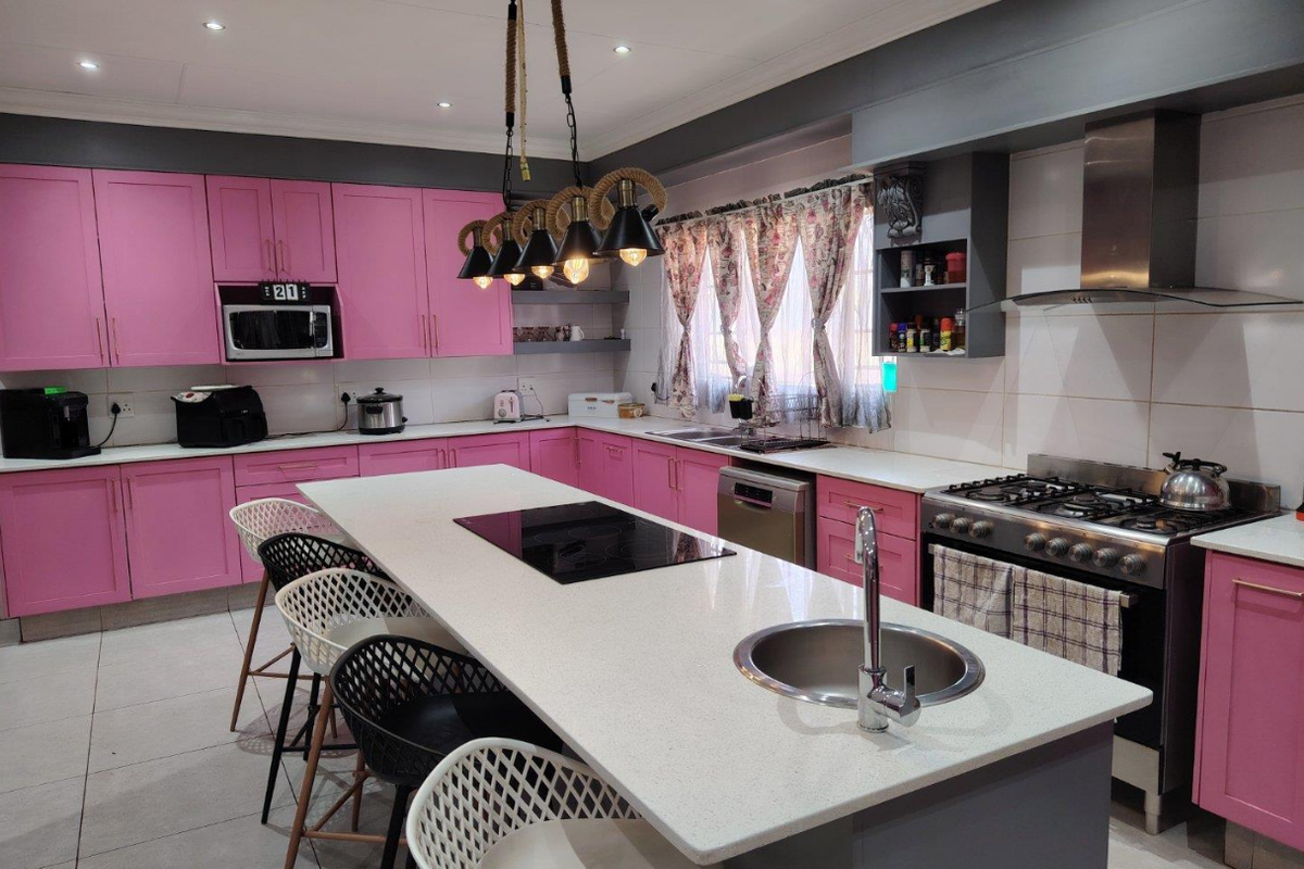 Spacious kitchen featuring pink cabinetry, a large central island with a gas hob and prep sink, quartz countertops, and modern stainless steel appliances.