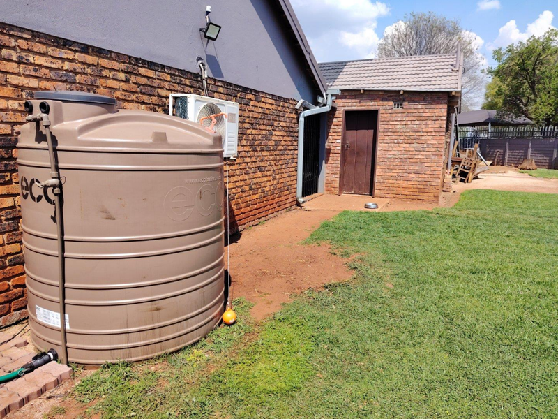 Rear exterior view of the property featuring a large water storage tank, air conditioning unit, and brick wall construction with a secure rear access door.