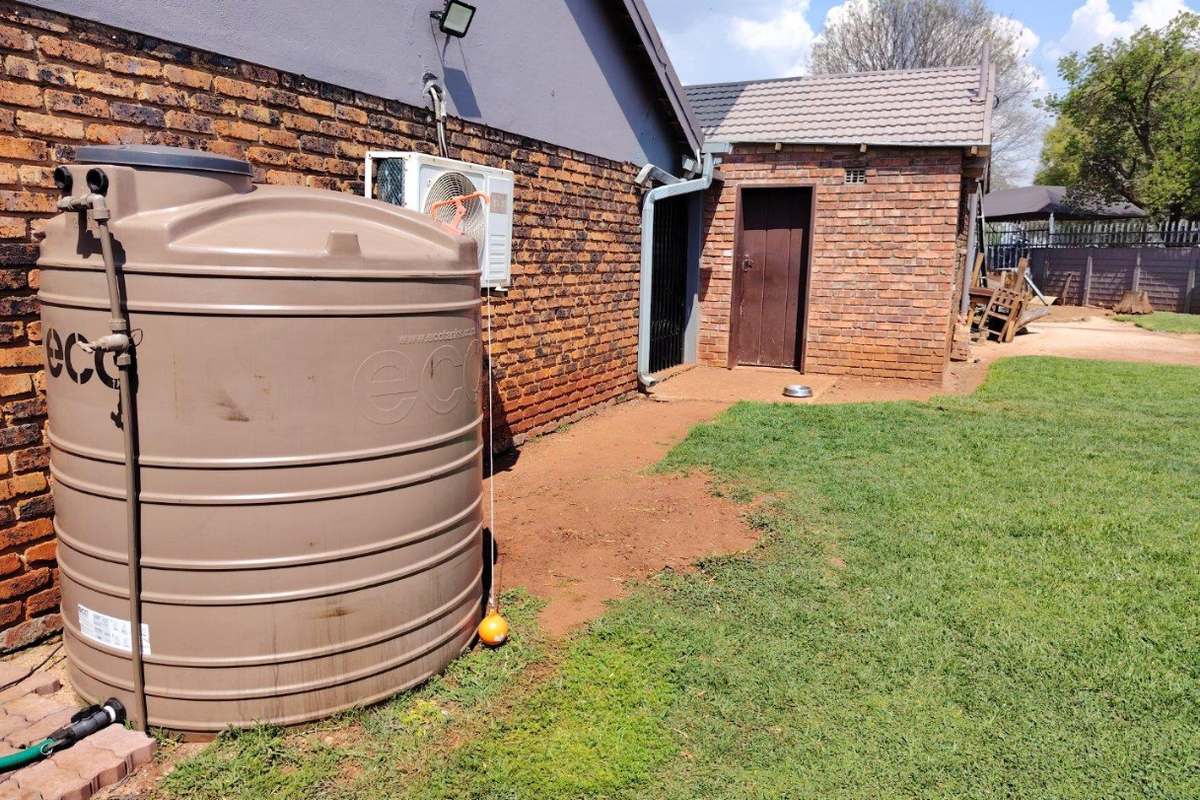 Rear exterior view of the property featuring a large water storage tank, air conditioning unit, and brick wall construction with a secure rear access door.