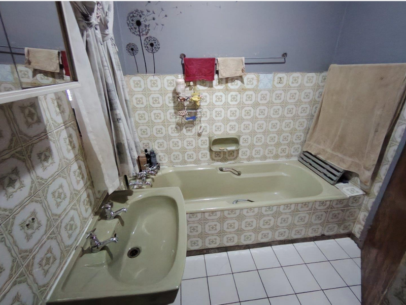 A dated bathroom featuring a built-in bathtub, pedestal basin, and patterned ceramic wall tiles. The space offers a functional layout ready for modernization.