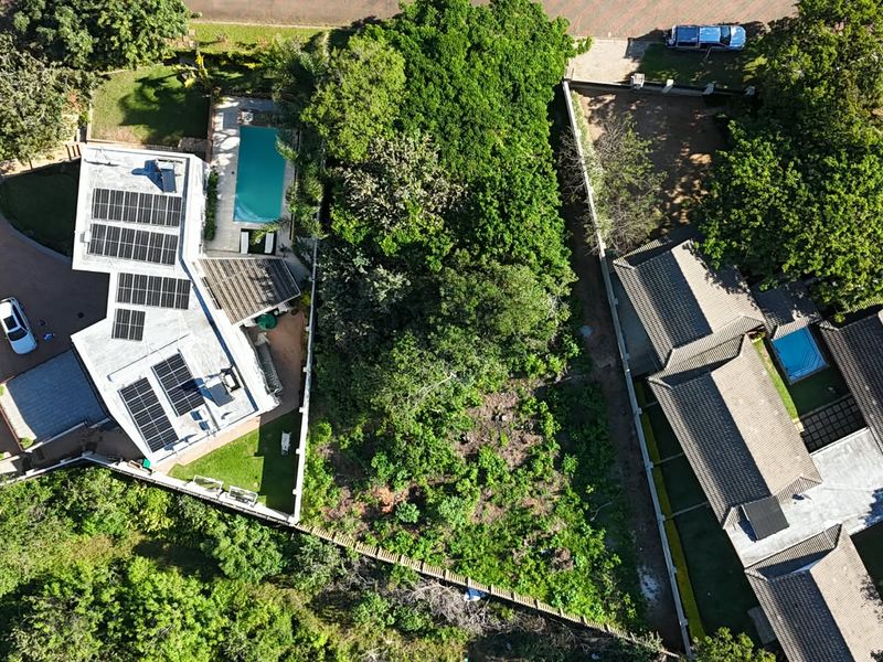 Aerial view of a residential property featuring a swimming pool, solar panel installation, and established garden areas within a fenced boundary.