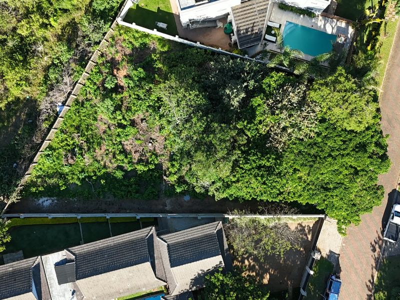 Aerial view of a vacant residential plot featuring dense vegetation, boundary fencing, and established retaining walls within a developed neighborhood.
