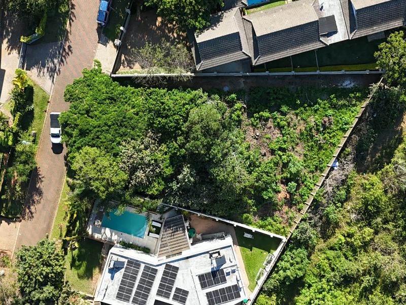 Aerial view of a vacant residential plot featuring established vegetation and boundary fencing, situated within an established neighborhood.