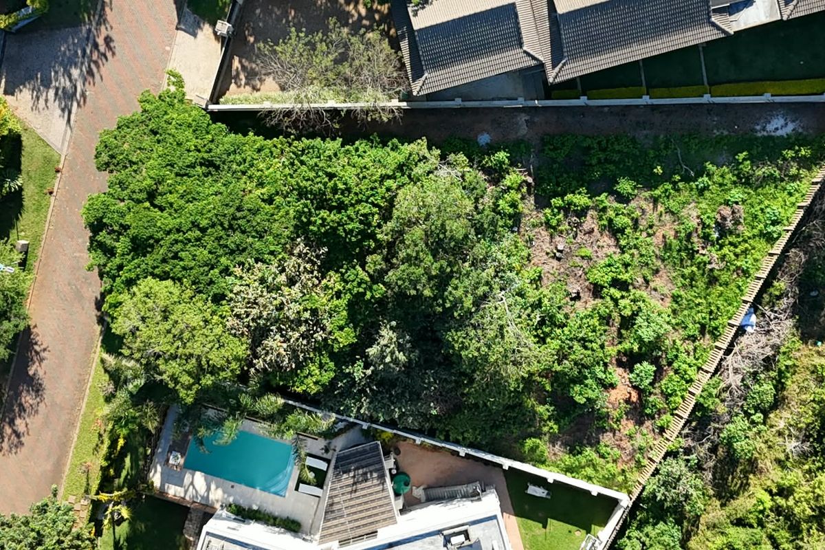 Aerial view of a residential vacant land plot featuring mature trees, a swimming pool, and boundary walling in a suburban setting.