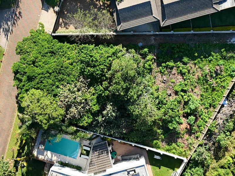 Aerial view of a residential vacant land plot featuring mature trees, a swimming pool, and boundary walling in a suburban setting.