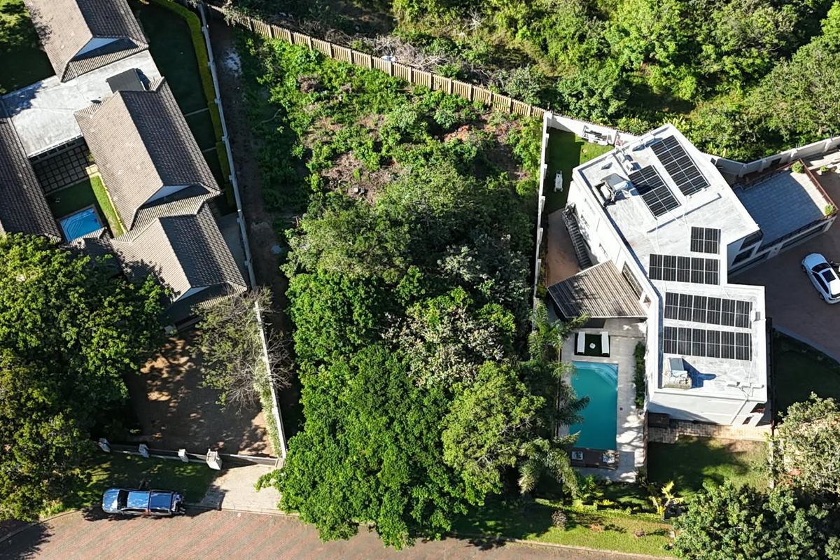 Aerial view of a residential property featuring a swimming pool, solar panel installation, and established garden surroundings.