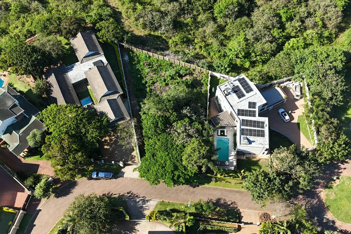 Aerial view of a residential property featuring a swimming pool, solar panel installation, and paved driveway within a landscaped estate setting.
