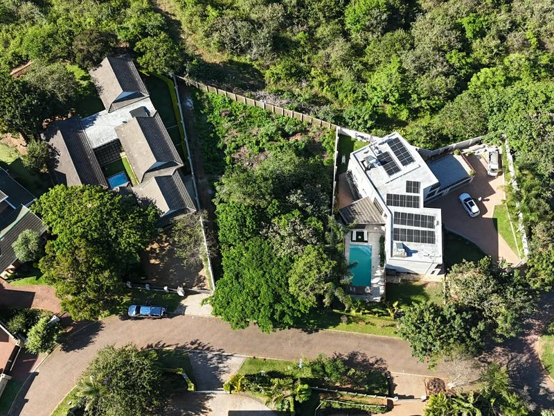 Aerial view of a residential property featuring a swimming pool, solar panel installation, and paved driveway within a landscaped estate setting.