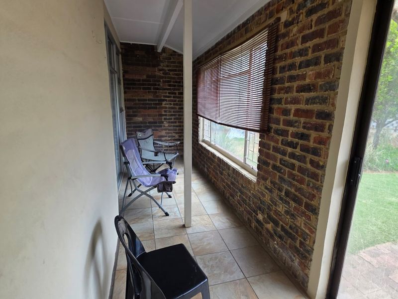 A covered patio area featuring exposed brick walls, tiled flooring, and large sliding glass doors providing access to the garden.