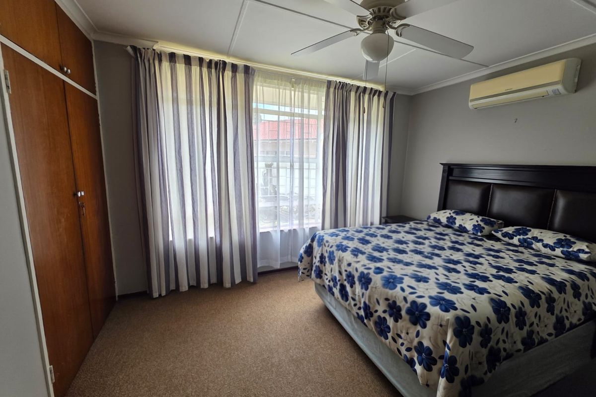 A functional bedroom featuring built-in wooden wardrobes, a ceiling fan, and a wall-mounted air conditioning unit, providing comfortable climate control.