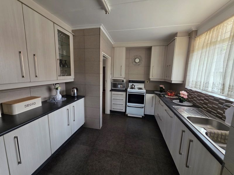 A functional kitchen featuring light wood-grain cabinetry, dark countertops, tiled backsplash, and a freestanding stove with ample storage space.