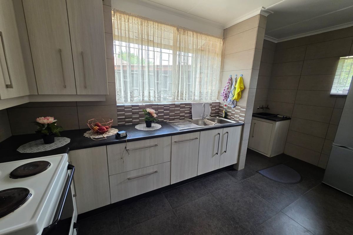 A functional kitchen featuring light wood-grain cabinetry, dark laminate countertops, tiled backsplash, and tiled flooring with a built-in sink and electric stove.