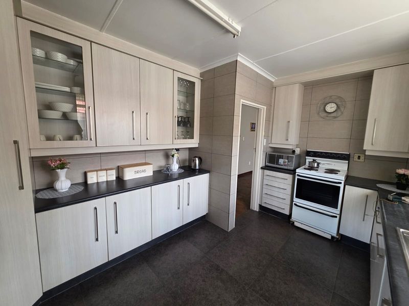 A functional kitchen featuring light wood-grain cabinetry, dark countertops, tiled flooring, and a freestanding stove with a tiled backsplash.