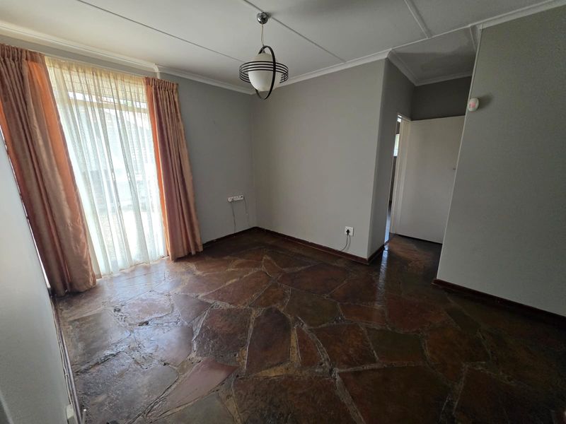 An empty living room featuring traditional flagstone flooring, a central light fixture, and a sliding glass door providing access to the exterior.