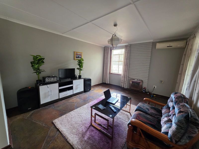A living room featuring natural stone flooring, a brick fireplace, and a wall-mounted air conditioning unit.