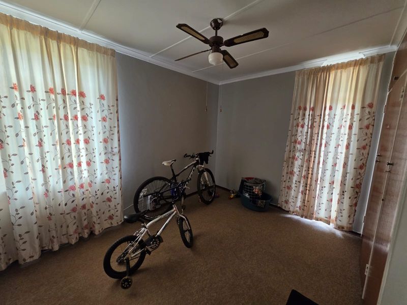 A spacious bedroom featuring neutral walls, carpeted flooring, and a ceiling fan, offering a blank canvas for personalization.