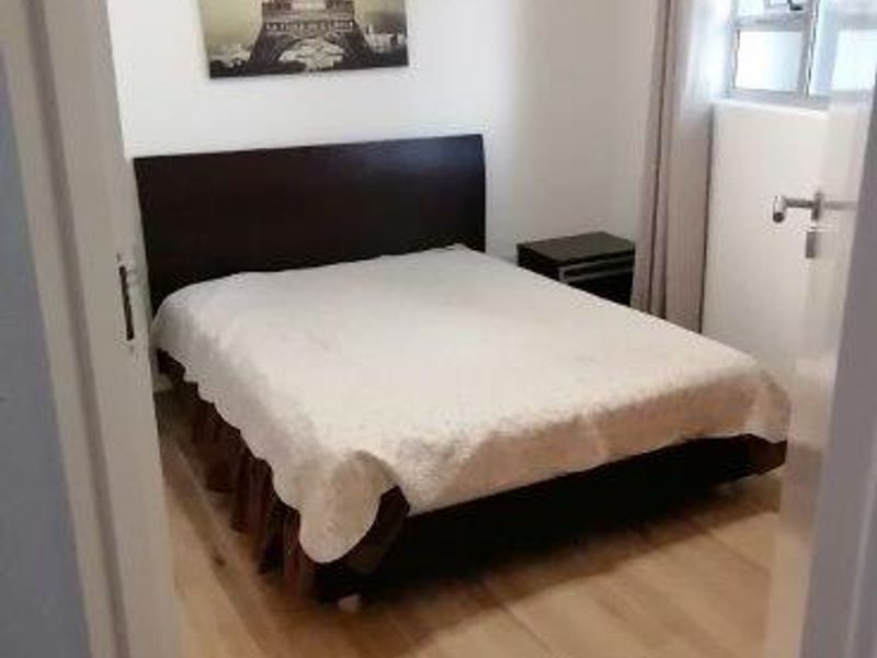 A functional bedroom featuring light-toned laminate flooring and a window, providing a neutral base for personalization.