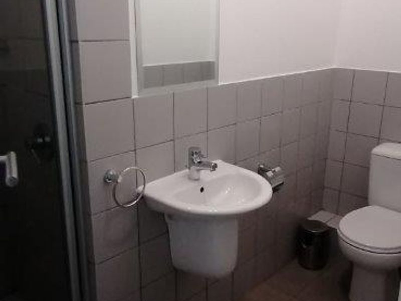A functional bathroom featuring a wall-mounted basin, a shower enclosure, and a toilet, finished with neutral wall and floor tiling.
