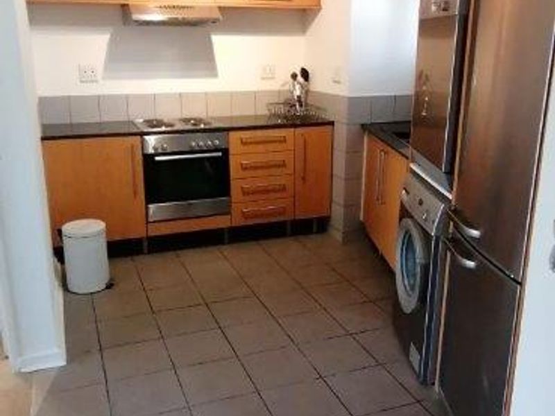 A functional kitchen featuring wooden cabinetry, built-in oven and hob, extractor fan, and tiled flooring with a neutral splashback.