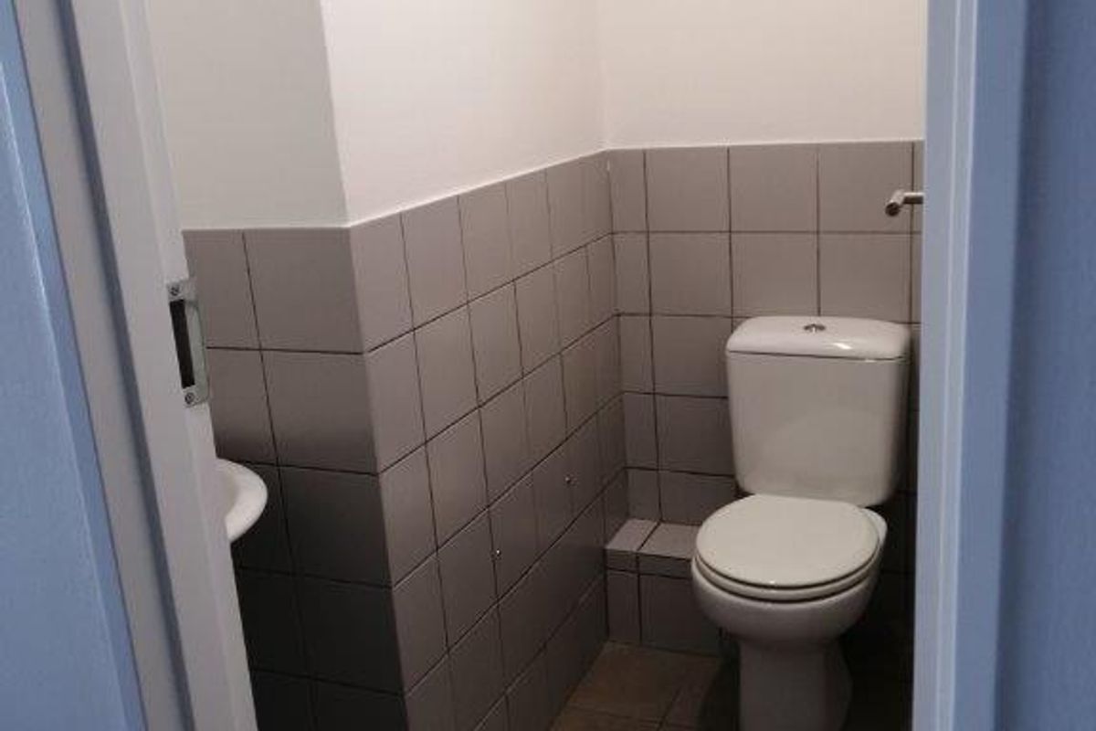 A compact bathroom featuring a white toilet, a small washbasin, and neutral grey ceramic wall and floor tiling.