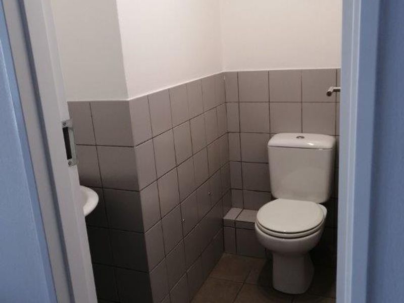 A compact bathroom featuring a white toilet, a small washbasin, and neutral grey ceramic wall and floor tiling.