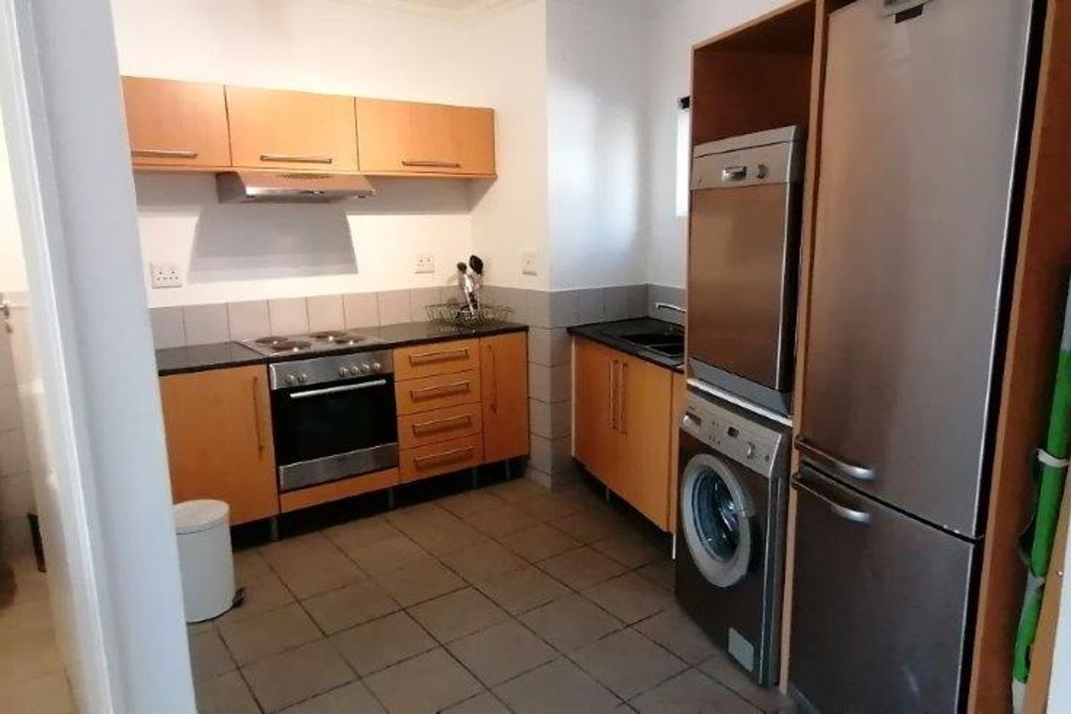 Functional kitchen featuring laminate cabinetry, built-in oven, hob, and extractor fan, with adjacent toilet and tiled flooring throughout.