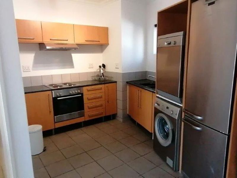 Functional kitchen featuring laminate cabinetry, built-in oven, hob, and extractor fan, with adjacent toilet and tiled flooring throughout.