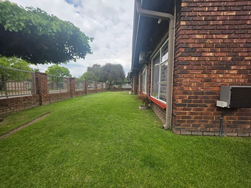A side view of the property showing a well-maintained lawn, brick exterior walls, and a secure perimeter fence.