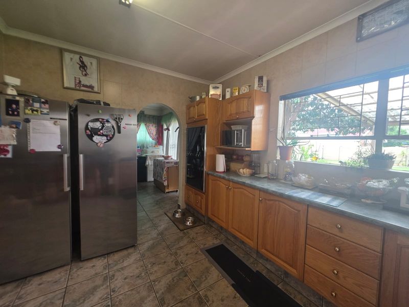 A functional kitchen featuring wooden cabinetry, laminate countertops, and tiled flooring, with an archway leading to an adjacent space.