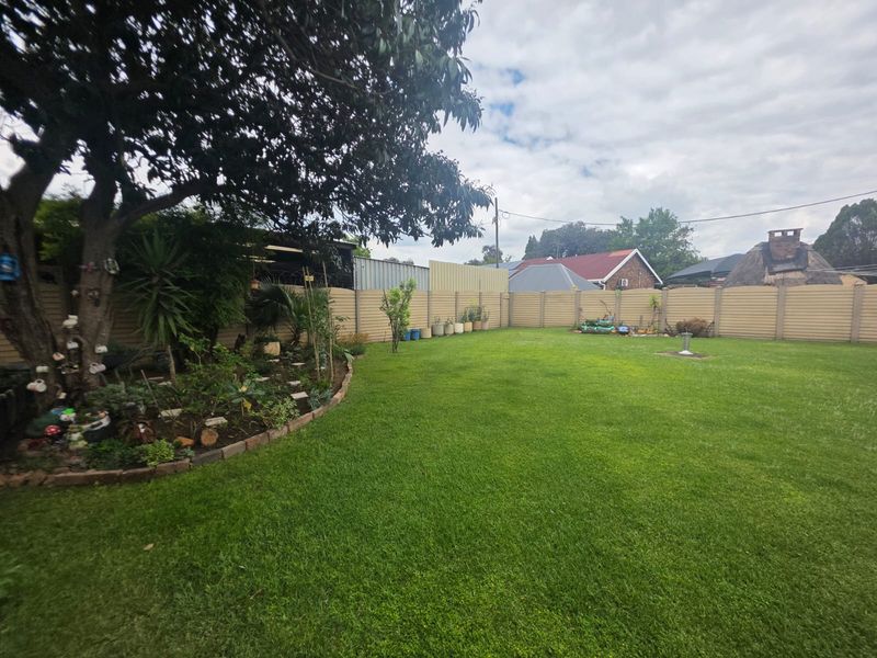A well-maintained private backyard featuring a lush green lawn, established tree, and secure precast concrete perimeter walling.