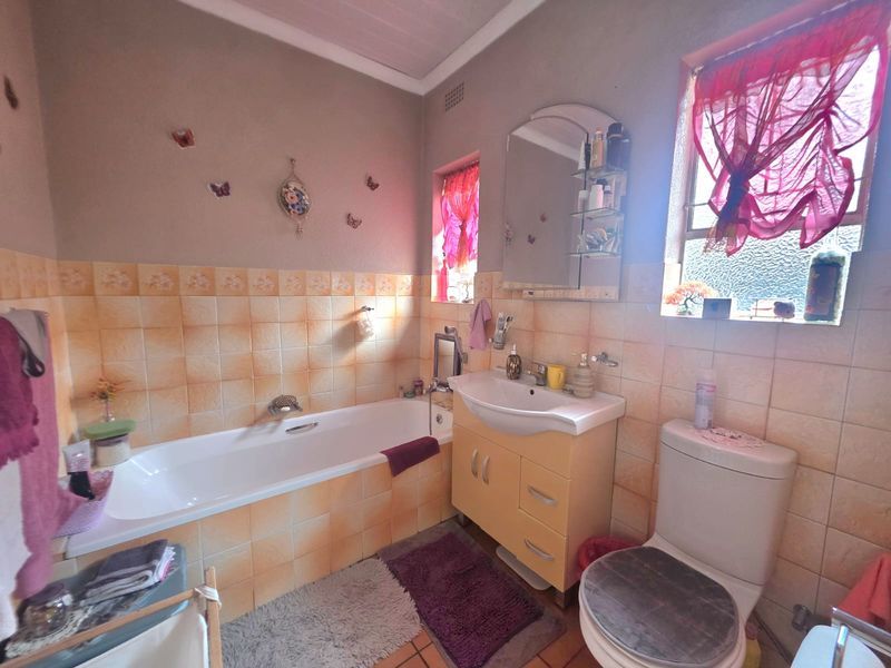 A functional bathroom featuring a built-in bathtub, vanity cabinet with integrated basin, and a standard toilet, finished with dated wall tiling.
