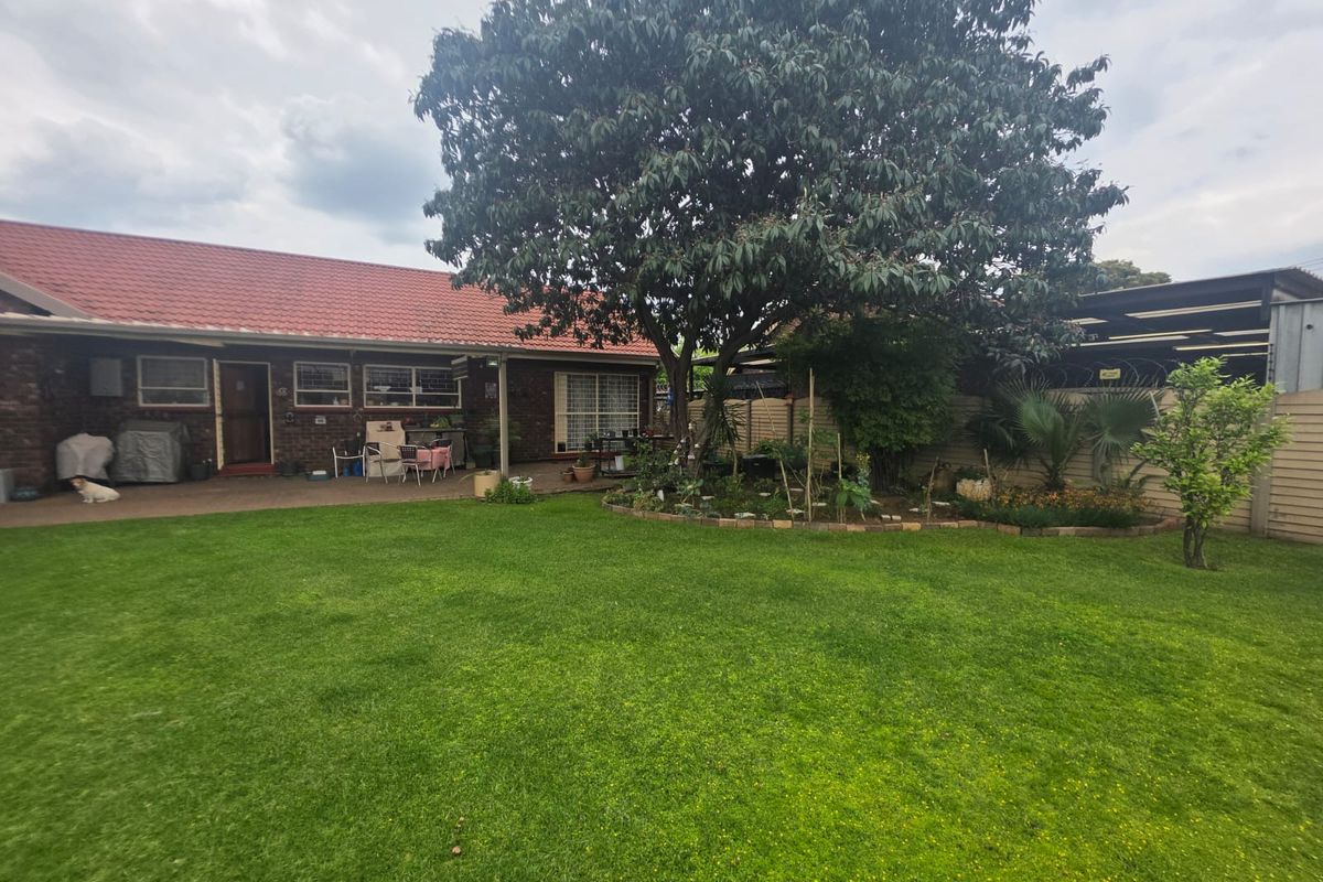 A spacious rear garden featuring a well-maintained lawn, mature tree, and a paved patio area adjacent to the brick-built house with a tiled roof.