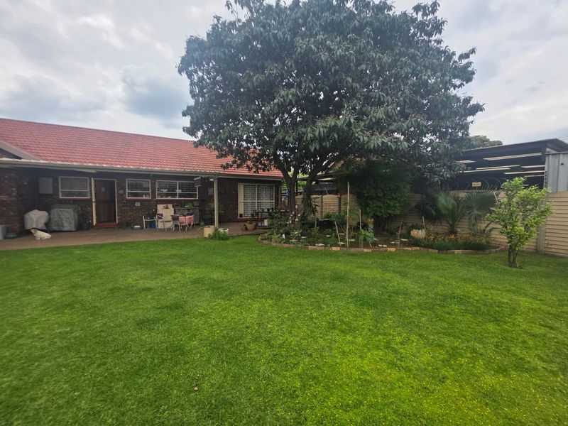 A spacious rear garden featuring a well-maintained lawn, mature tree, and a paved patio area adjacent to the brick-built house with a tiled roof.