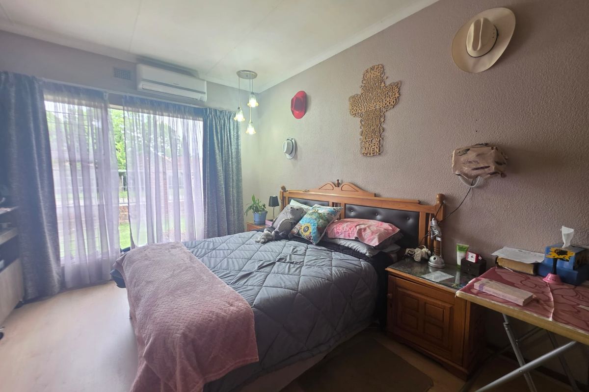 A comfortable bedroom featuring laminate flooring, a wall-mounted split-system air conditioner, and large sliding glass doors providing natural light.
