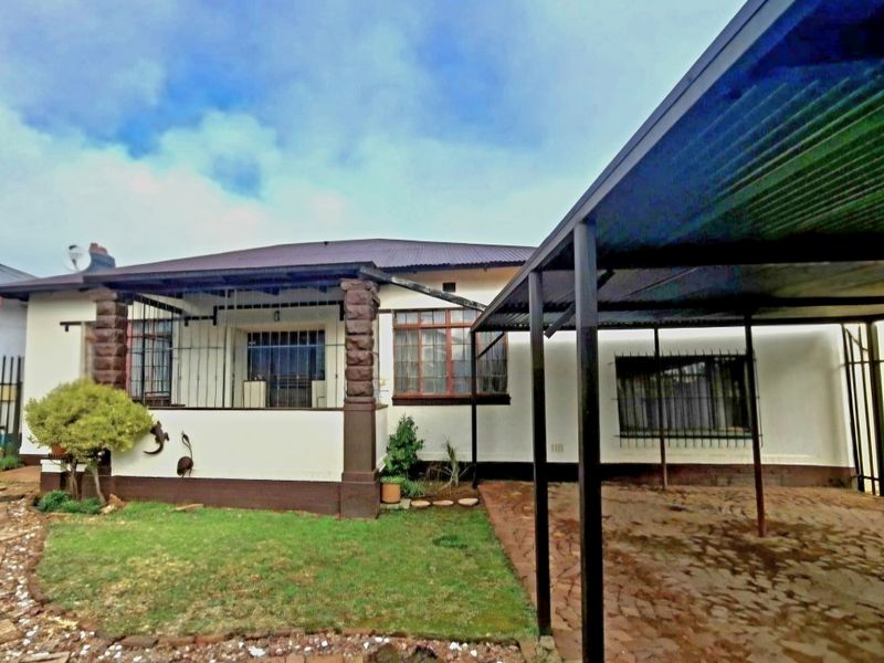 Front elevation of a house featuring a covered patio with stone-clad pillars, a paved carport, and security bars on windows.