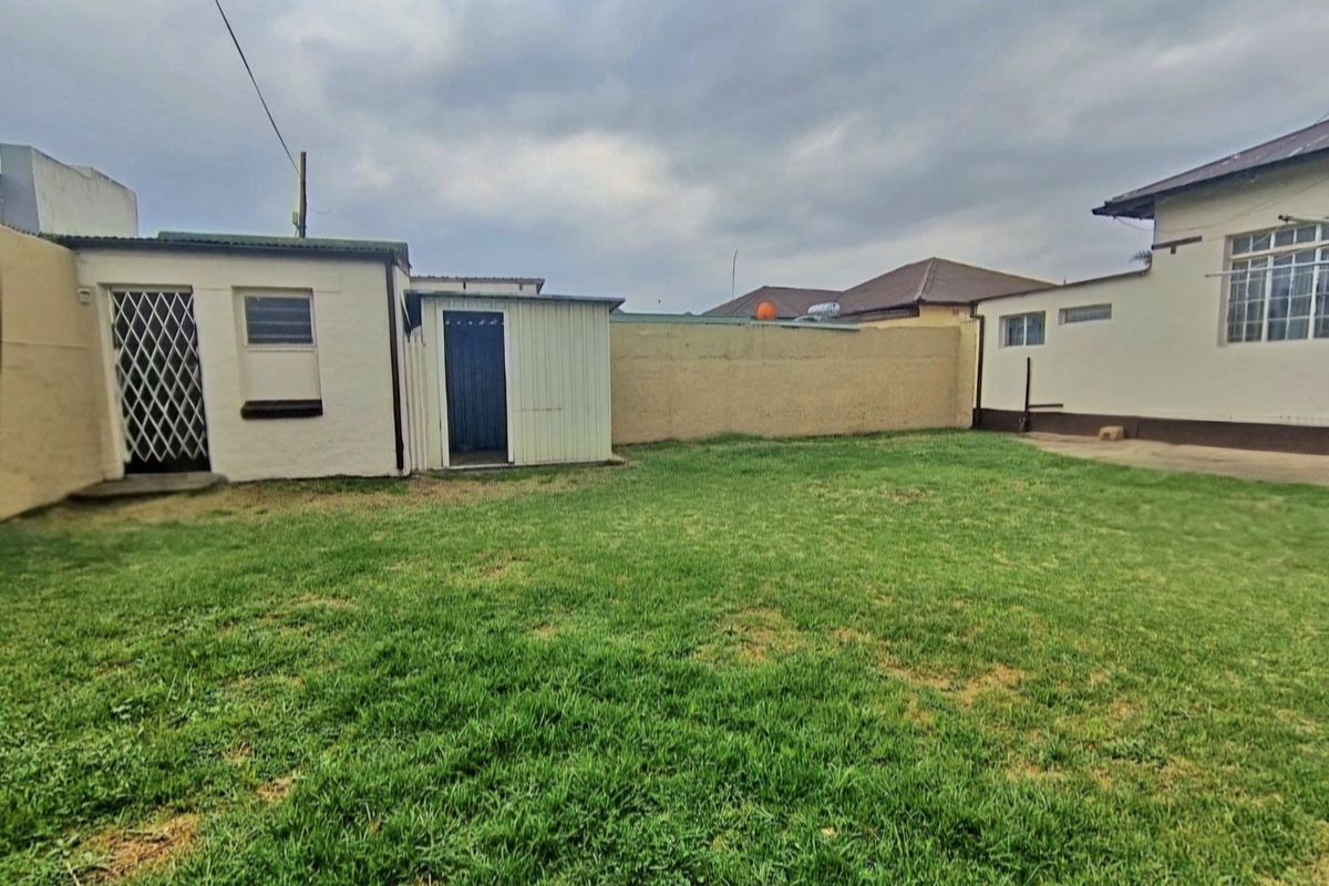 A rear garden view featuring a lawn, perimeter boundary wall, and an outbuilding with a security gate.