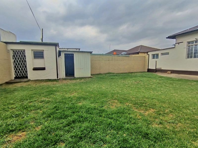 A rear garden view featuring a lawn, perimeter boundary wall, and an outbuilding with a security gate.