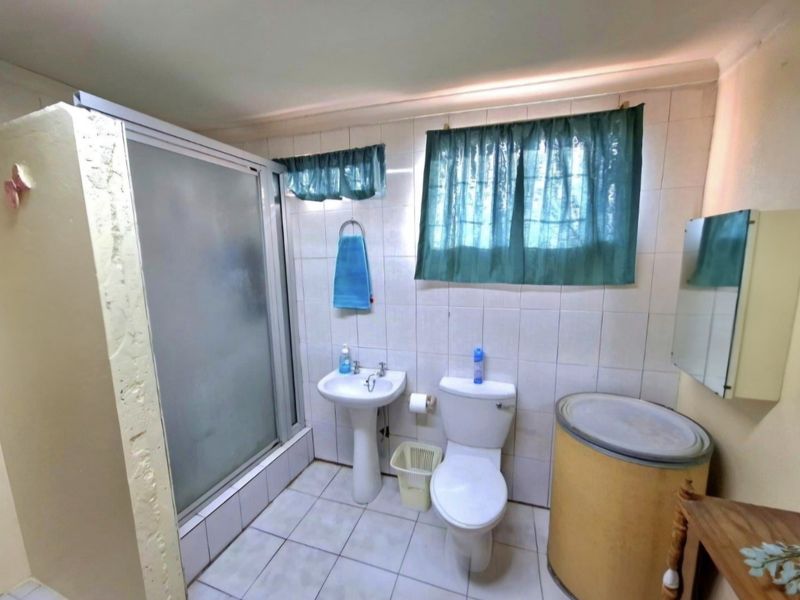 A functional bathroom featuring a shower enclosure, pedestal basin, and toilet with tiled finishes throughout.