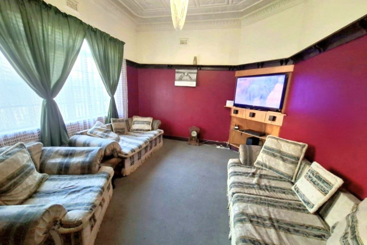 A living room featuring an ornate pressed metal ceiling, picture rails, and a built-in media console, requiring cosmetic updates to modernize the space.