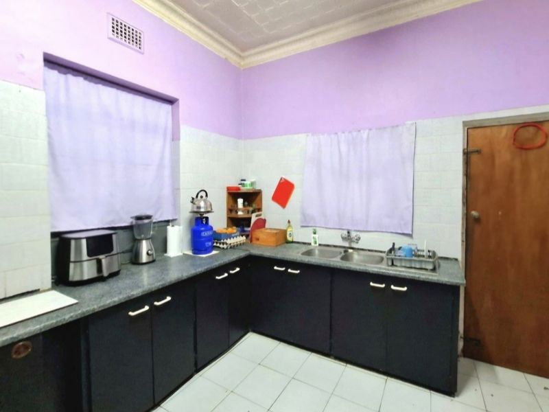 A functional kitchen featuring dark cabinetry, a double basin sink, tiled splashbacks, and tiled flooring, offering a practical layout with potential for modern updates.