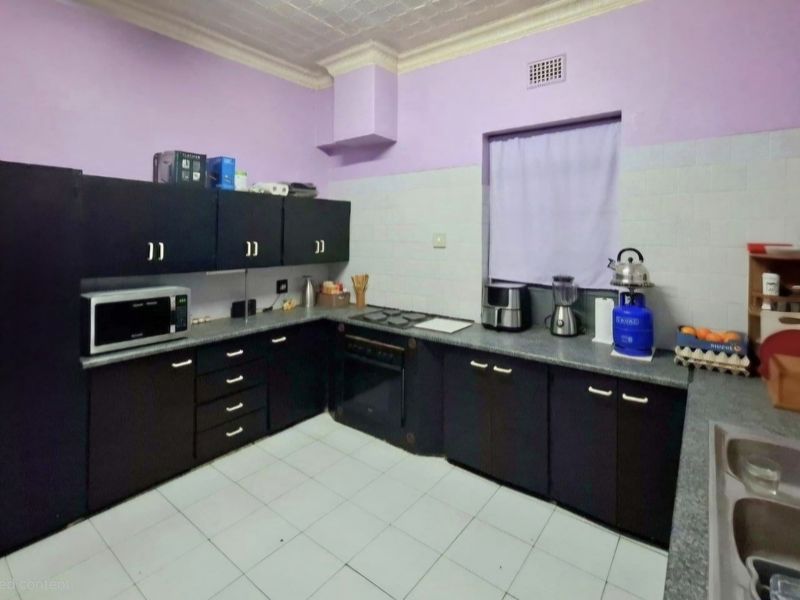 A functional kitchen featuring dark built-in cabinetry, laminate countertops, a built-in oven with hob, and a double bowl sink with tiled backsplash.
