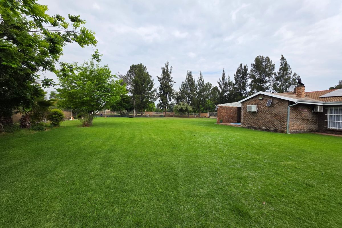 A spacious rear garden featuring a well-maintained lawn, brick exterior facade, and established trees, providing a private outdoor area.