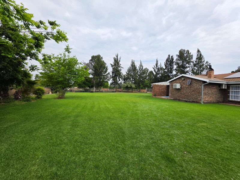 A spacious rear garden featuring a well-maintained lawn, brick exterior facade, and established trees, providing a private outdoor area.
