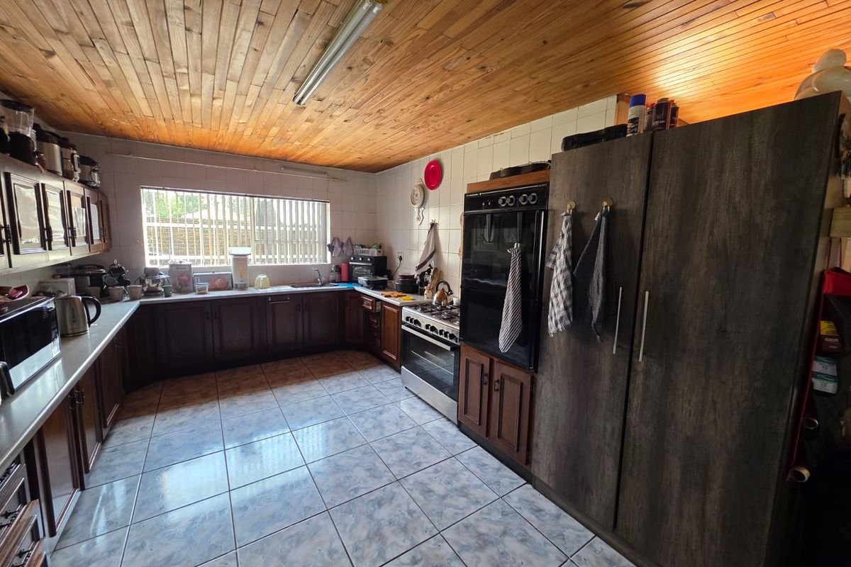 A functional kitchen featuring timber ceiling paneling, tiled flooring, built-in cabinetry, and integrated oven and hob appliances.