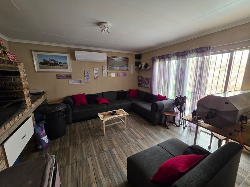 A living room featuring tiled flooring, a built-in brick fireplace, and a wall-mounted air conditioning unit with access to an outdoor area via sliding doors.
