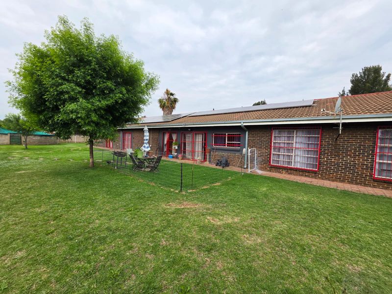 Rear view of a single-story brick house featuring a tiled roof with solar panels, security bars on windows, and a spacious garden area.