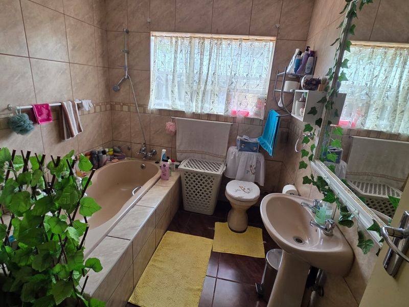 A functional bathroom featuring a built-in bathtub, pedestal basin, and toilet with neutral wall and floor tiling.